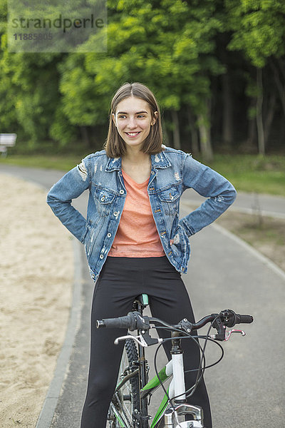 Lächelnde Frau mit Händen an der Hüfte auf dem Fahrrad auf der Straße sitzend