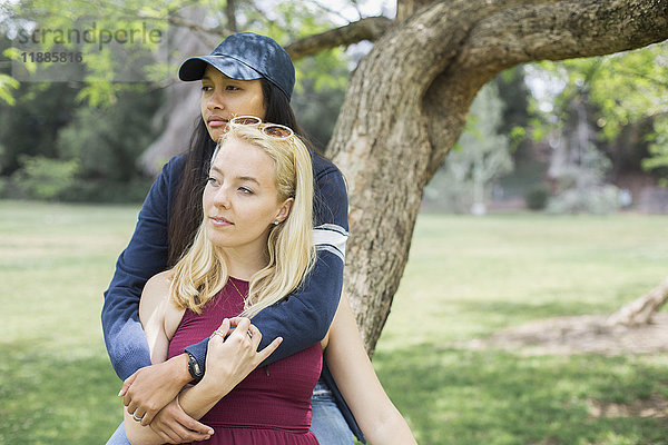 Zwei junge Frauen sitzen zusammen auf einem Baumstamm im Park.