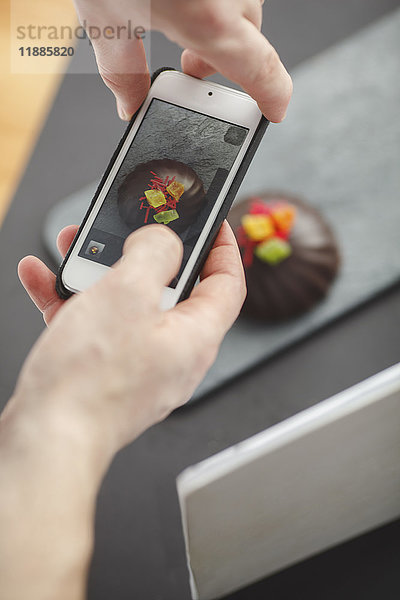 Beschnittenes Bild eines Mannes  der das Dessert auf dem Tisch mit dem Handy fotografiert.