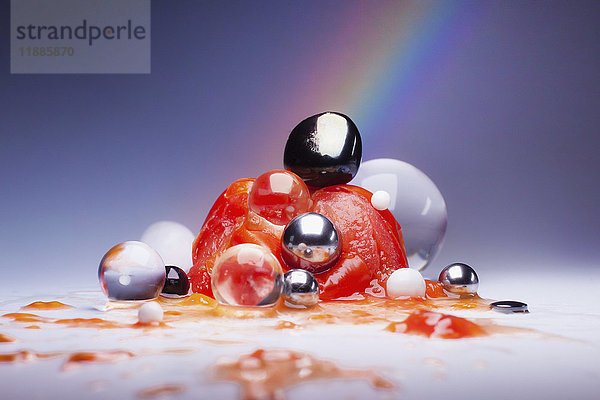 Zerschmetterte Tomate über glänzenden Murmeln und Kugeln vor mehrfarbigem Hintergrund