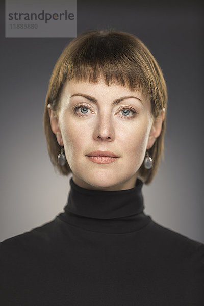 Porträt einer mittelgroßen Frau mit kurzen braunen Haaren auf grauem Hintergrund