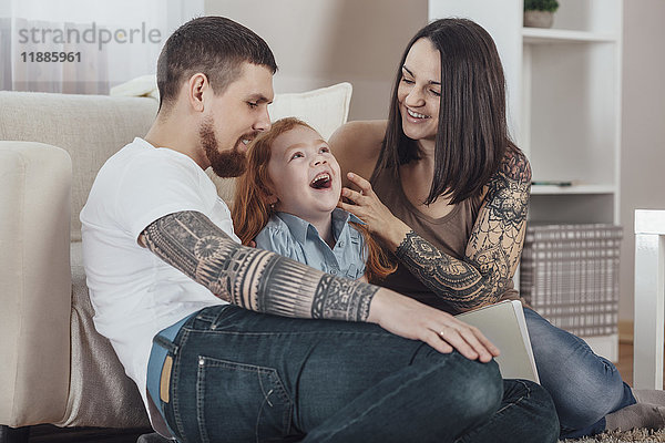 Fröhliche Eltern spielen mit der Tochter auf dem Sofa im Wohnzimmer zu Hause