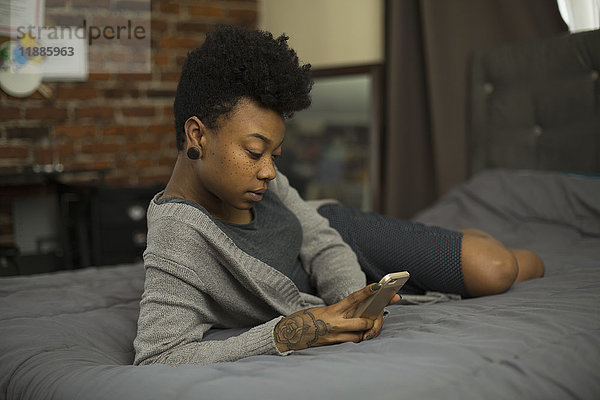 Junge Frau  die das Telefon benutzt  während sie zu Hause auf dem Bett liegt.