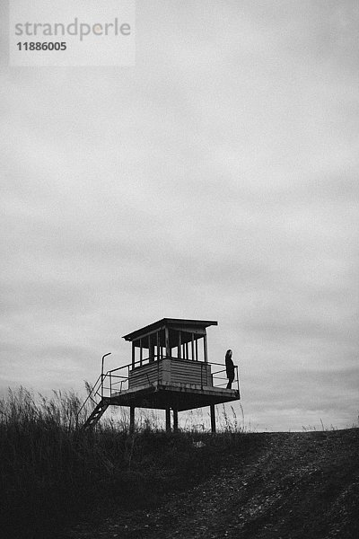 Fernsicht des Teenagers auf dem Aussichtsturm auf dem Feld gegen den Himmel