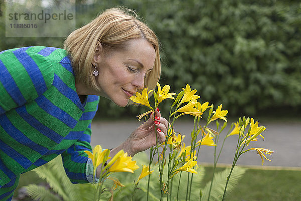 Seitenansicht einer reifen Frau  die im Park gelbe Blumen riecht.