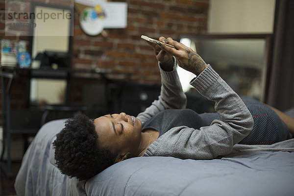 Junge Frau auf dem Bett liegend mit dem Handy zu Hause