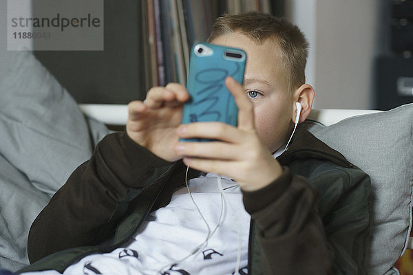 Junge hört Musik  während er zu Hause mit dem Smartphone telefoniert.