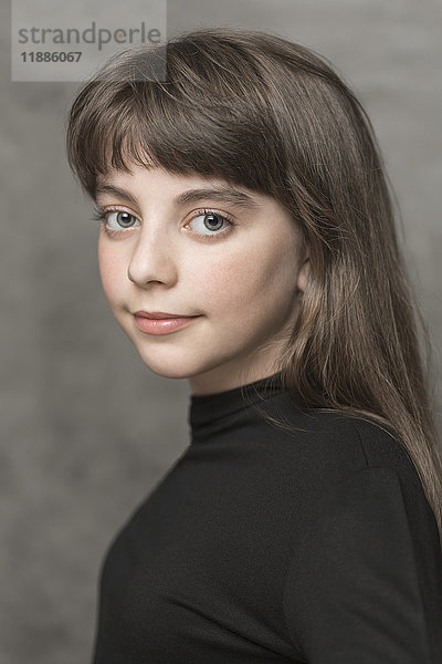 Seitenansicht Porträt eines lächelnden Mädchens mit langen Haaren vor grauem Hintergrund