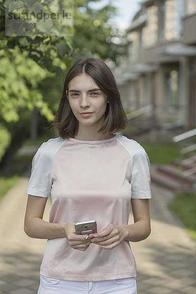 Porträt einer lächelnden jungen Frau mit einem Smartphone auf dem Bürgersteig