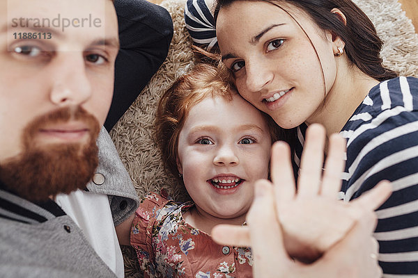 Hochwinkel-Porträt einer lächelnden Familie  die zu Hause auf einem Teppich liegt.