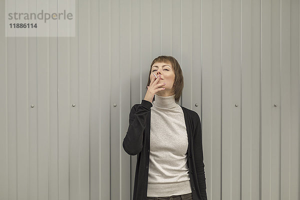 Mittlere erwachsene Frau raucht Zigarette  während sie an der Wand steht.