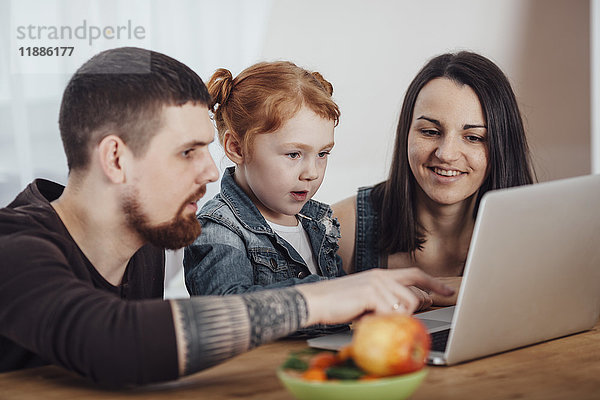 Eltern zeigen Laptop zu Tochter am Tisch im Wohnzimmer