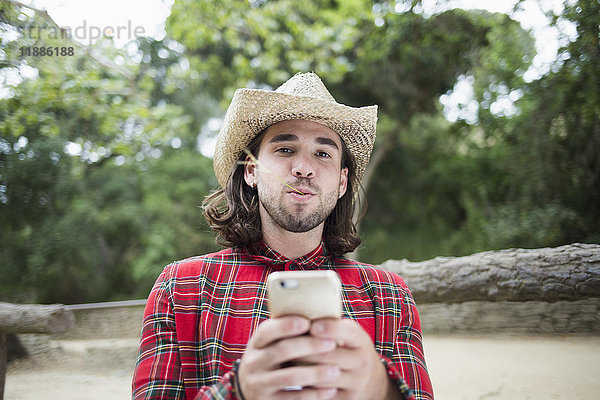 Porträt eines Mannes mit Zweig im Mund  der ein Smartphone im Park hält.