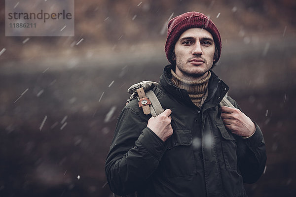 Porträt eines Mannes mit Rucksack  der bei Schneefall im Freien steht.