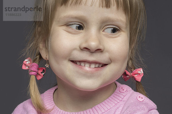 Nahaufnahme des süßen  lächelnden Mädchens mit rosa Pullover auf grauem Hintergrund