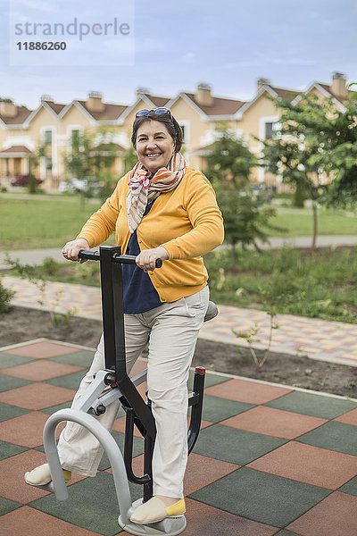 Volle Länge der lächelnden Seniorin mit Trainingsgeräten im Park