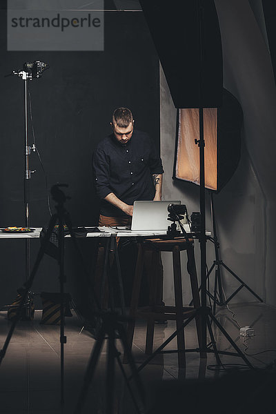 Fotograf  der am Laptop arbeitet  während er vor der Kulisse des Studios steht.