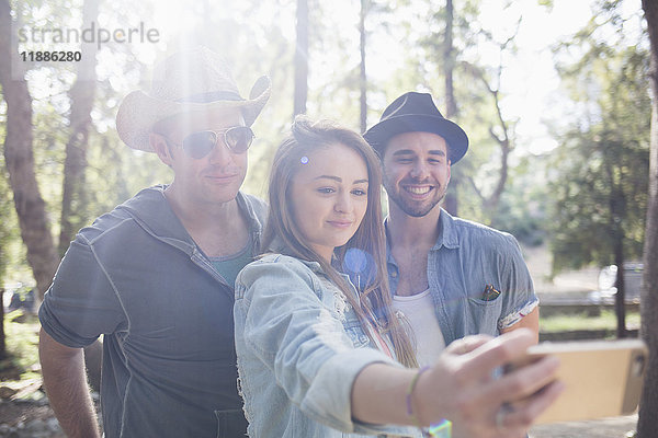 Schöne Frau nimmt Selfie mit männlichen Freunden durch Smartphone im Park während des sonnigen Tages.