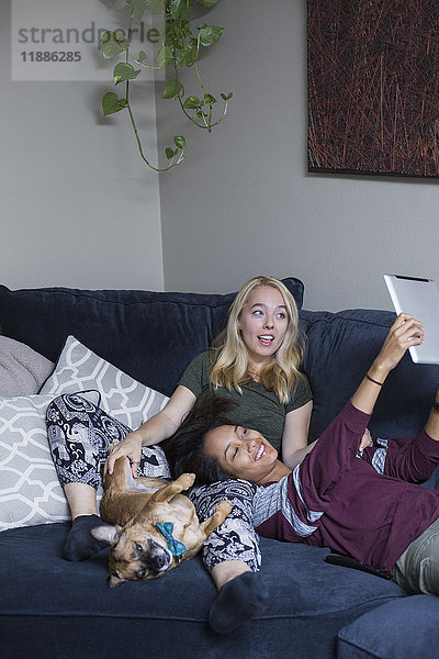 Glückliche Frau nimmt Selfie mit Freundin und Hund auf dem Sofa zu Hause.