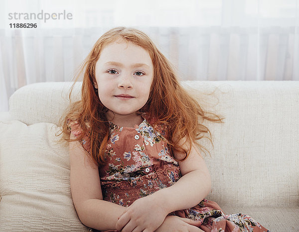 Porträt eines lächelnden Mädchens mit Rothaarigen  das zu Hause auf dem Sofa sitzt.
