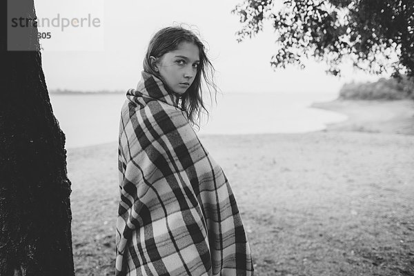 Porträt eines jungen Mädchens in Decke gehüllt am Seeufer stehend