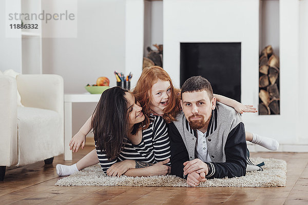 Porträt einer fröhlichen Tochter mit auf Teppich liegenden Eltern im Wohnzimmer zu Hause