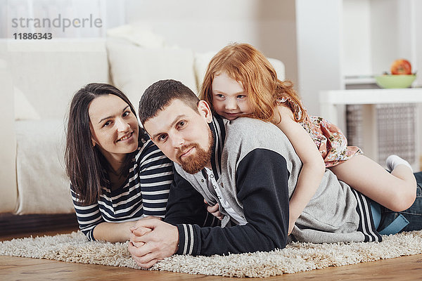 Porträt einer lächelnden Familie  die zu Hause auf einem Teppich liegt.