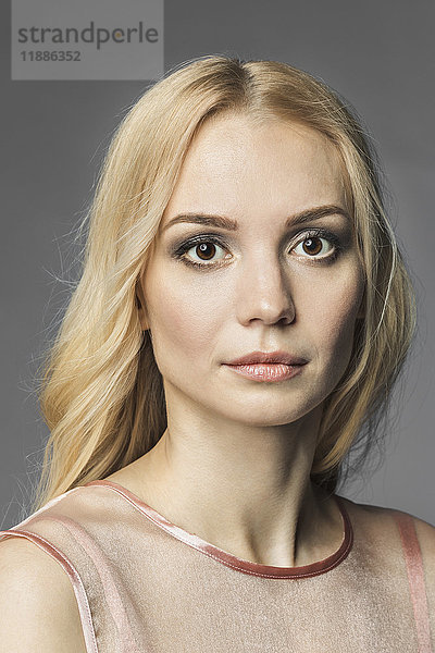 Porträt einer schönen jungen Frau mit blonden Haaren vor grauem Hintergrund