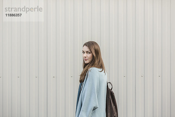 Porträt einer schönen jungen Frau  die einen Rucksack trägt  während sie an der Wand steht