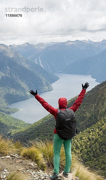 Wanderin mit Blick auf den South Fiord des Lake Te Anau  Arme ausgestreckt  Southern Alps im Rücken  Wanderweg Kepler Tack  Fiordland National Park  Southland  Neuseeland  Ozeanien