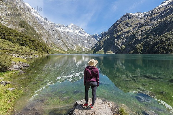 Weiblicher Wanderer mit Sonnenhut am Ufer stehend  Lake Marian  Fiordland National Park  Te Anau  Southland  Südinsel  Neuseeland  Ozeanien