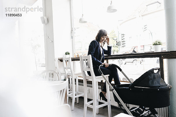 Geschäftsfrau arbeitet vom Café aus mit Kinderwagen an ihrer Seite