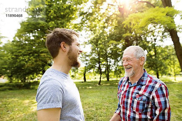 Seniorenvater und sein erwachsener Sohn lachen zusammen in einem Park.
