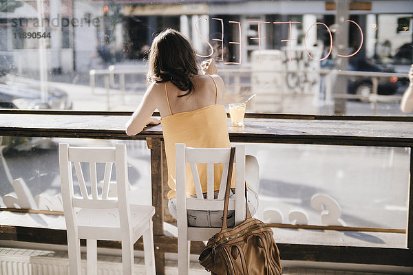 Frau sitzt im Café und schreibt das Wort Kaffee auf die Fensterscheibe.