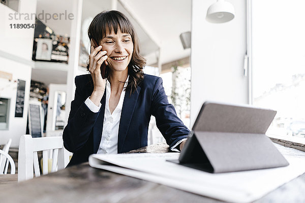 Geschäftsfrau sitzend im Café mit digitalem Tablett  telefonierend