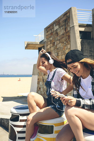 Zwei fröhliche junge Frauen  die Musik hören und Spaß am Strand haben.