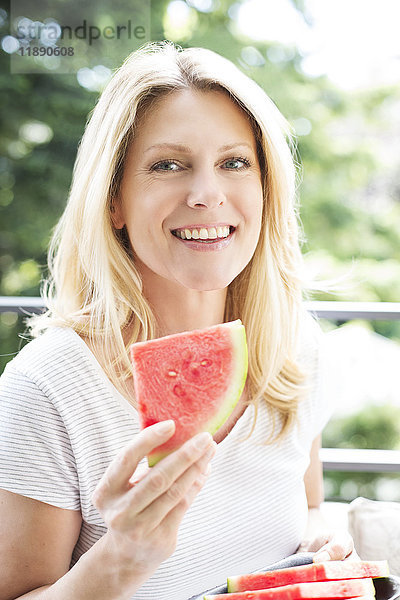 Reife Frau sitzt auf dem Balkon  isst Wassermelone  Porträt