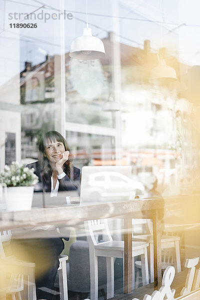 Geschäftsfrau sitzend im Café mit Laptop  lächelnd und denkend