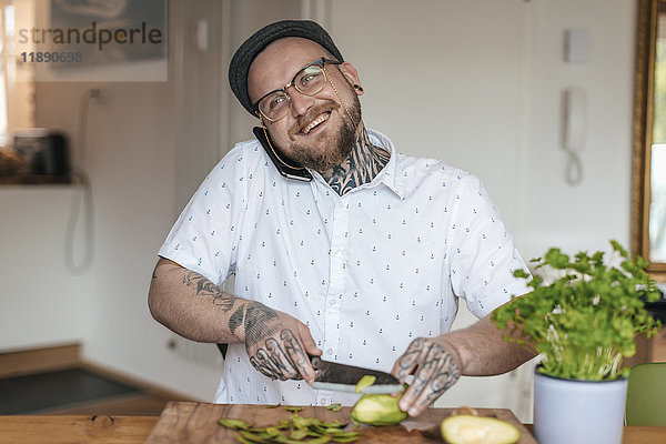 Lächelnder Mann am Telefon beim Gemüsehacken in der Küche