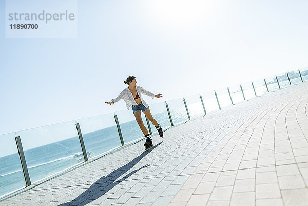 Junge Frau beim Inline-Skaten auf der Strandpromenade an der Küste