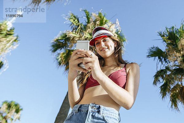 Junge Frau mit Sonnenblende und Bikini per Handy