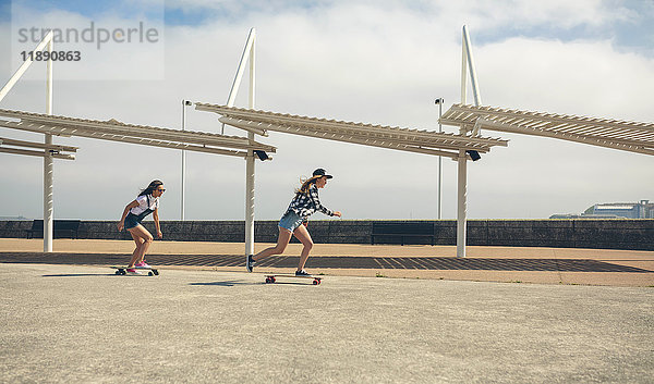 Zwei junge Frauen beim Longboarding an der Strandpromenade