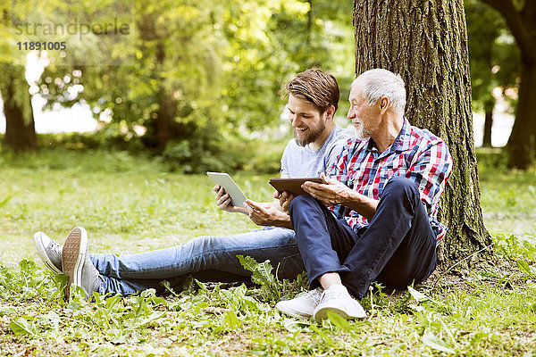 Senior Vater sitzt neben seinem erwachsenen Sohn in einem Park mit Tablette