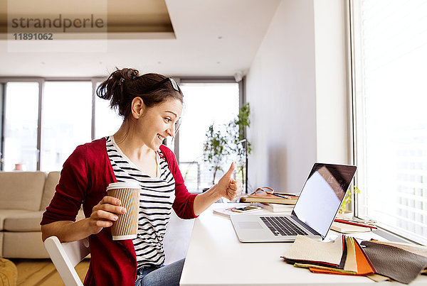 Lächelnde Frau mit Kaffee für zu Hause am Schreibtisch