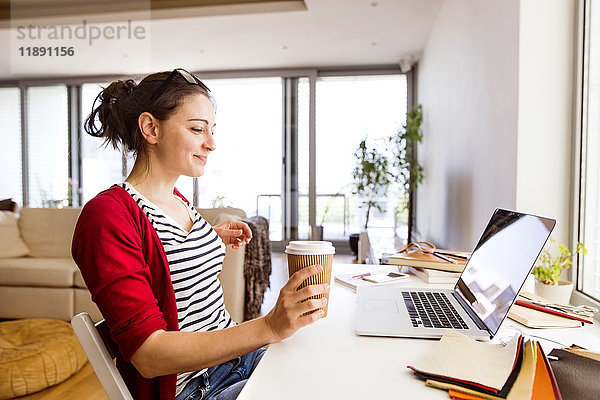 Lächelnde Frau mit Kaffee zum Mitnehmen im Home Office