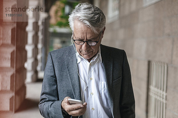 Senior Geschäftsmann mit Kopfhörern beim Blick auf das Handy