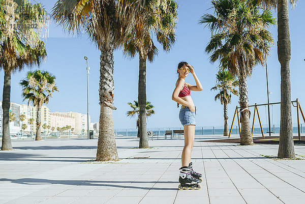 Junge Frau auf Inline-Skates auf einer Strandpromenade mit Palmen