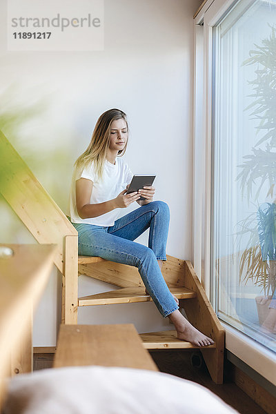 Junge Frau sitzt zu Hause mit digitalem Tablett