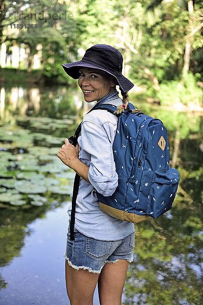 Porträt einer lächelnden Frau mit Rucksack vor einem See stehend