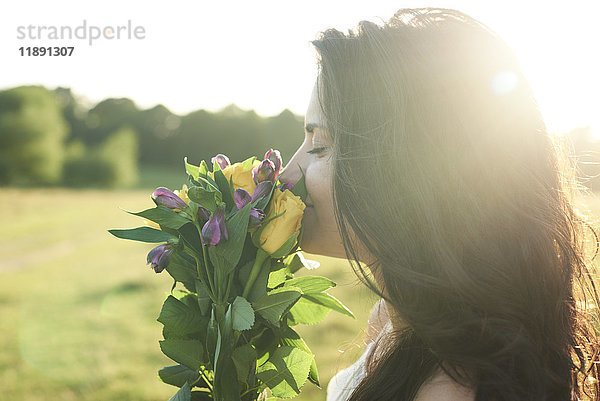 Profil einer jungen Frau  die bei Sonnenuntergang einen Blumenstrauß riecht.